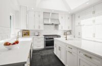 Bright white kitchen design with dark gray tiled floors. The cabinetry features modern shaker doors with a crisp, pure white paint color.