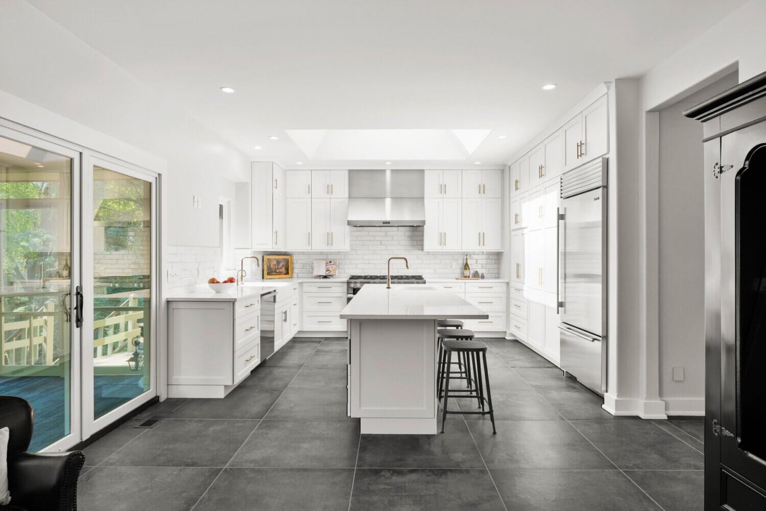 An all white kitchen with white cabinets, counters, and backsplash with a unique mix of metal finishes including brass cabinet hardware and stainless steel appliances.