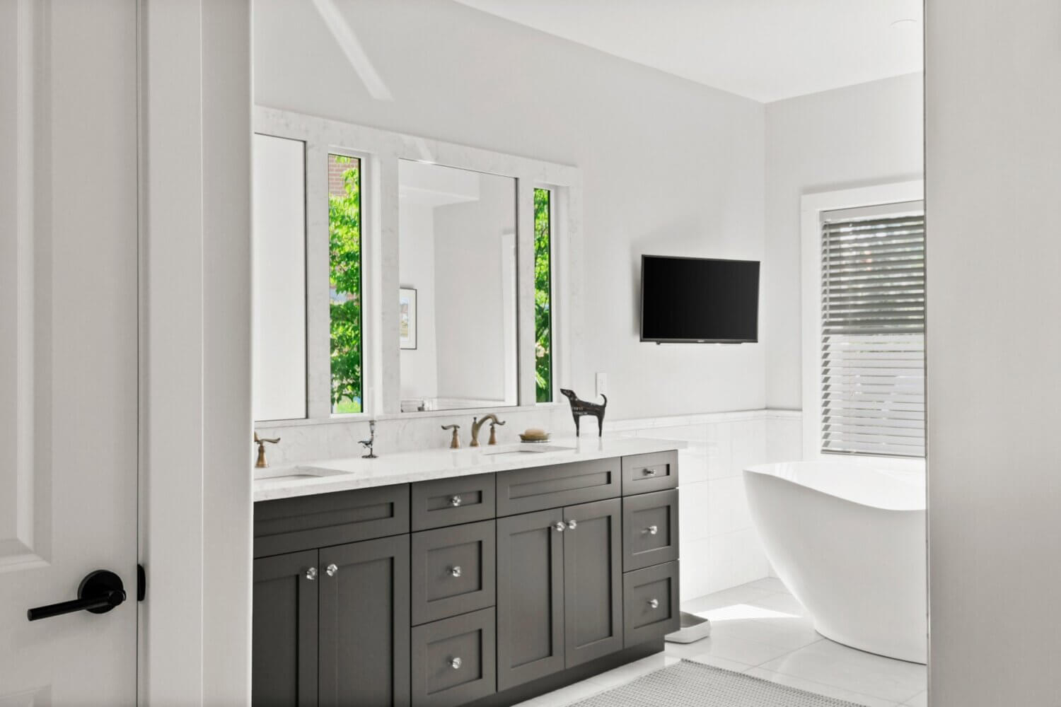 A bright white master bathroom design with a dark, charcoal graphite gray painted vanity with two sinks.