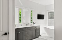 A bright white master bathroom design with a dark, charcoal graphite gray painted vanity with two sinks.