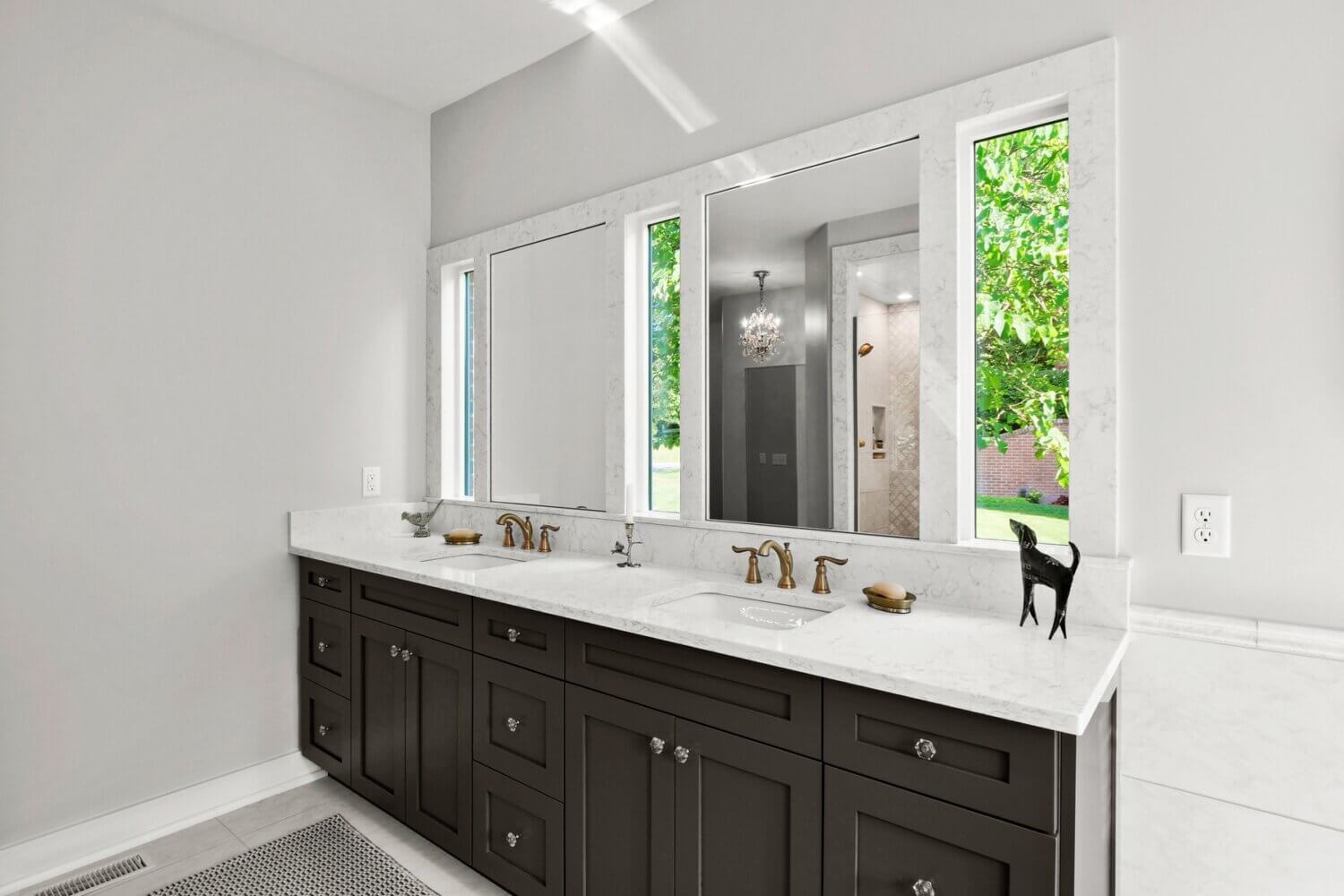 This black and white master bathroom has natural light pooling through the windows behind the vanity mirrors and a dark gray painted vanity.