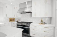 An all white kitchen with shaker cabinetry from Dura Supreme Cabinetry, brass hardware, and stainless steel appliances.