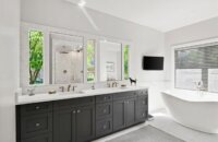 A black and white bathroom with a long double sink vanity in a dark gray paint with shaker doors.