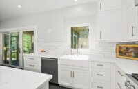 This all white kitchen uses pure white for the flat panel door cabinets, the apron sink, subway tile backsplash, countertops, etc.
