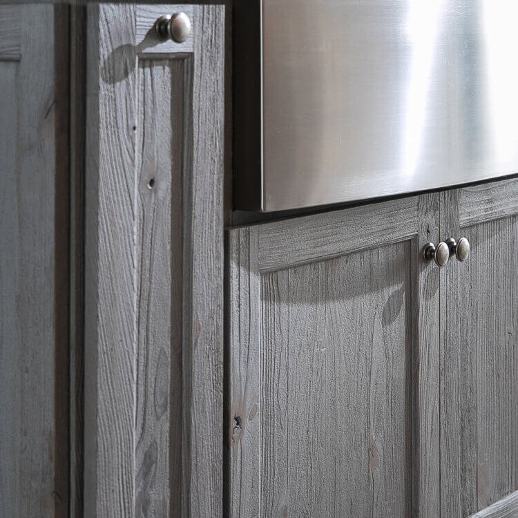 A close up of a sink base cabinet in a kitchen island with rustic, weathered wood cabinetry in a gray stained finish.
