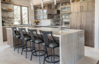 This modern kitchen has a waterfall kitchen island, seating for four, and stunning light gray-brown stained cabinets from Dura Supreme.