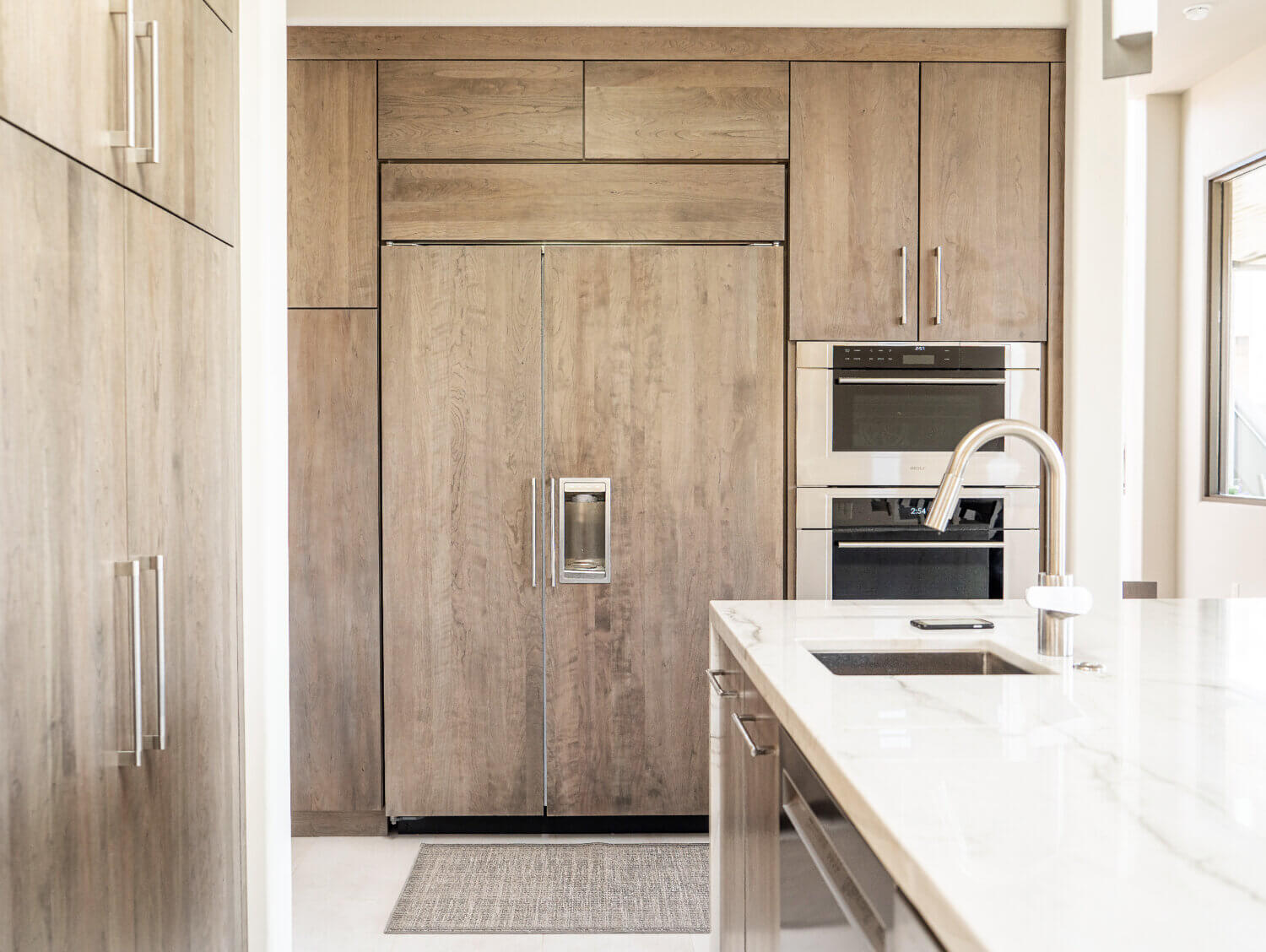 A full wall of light gray-brown stained cabinets with slab doors and a hidden appliance paneled fridge.