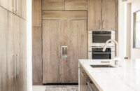 A full wall of light gray-brown stained cabinets with slab doors and a hidden appliance paneled fridge.