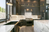 This modern kitchen has a large window view at the black kitchen sink, tall ceilings, and sleek black textured cabinets.