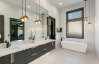 A sleek, modern bathroom design with a black and white color palette and premium contemporary materials and finishes. The long stretching black cabinetry is wall-hung to look as if it’s floating above the bathroom floor delivers heaps of drama to this master bathroom featuring Dura Supreme’s black “Basalt” Textured TFL on the Tempo-Vertical door style.