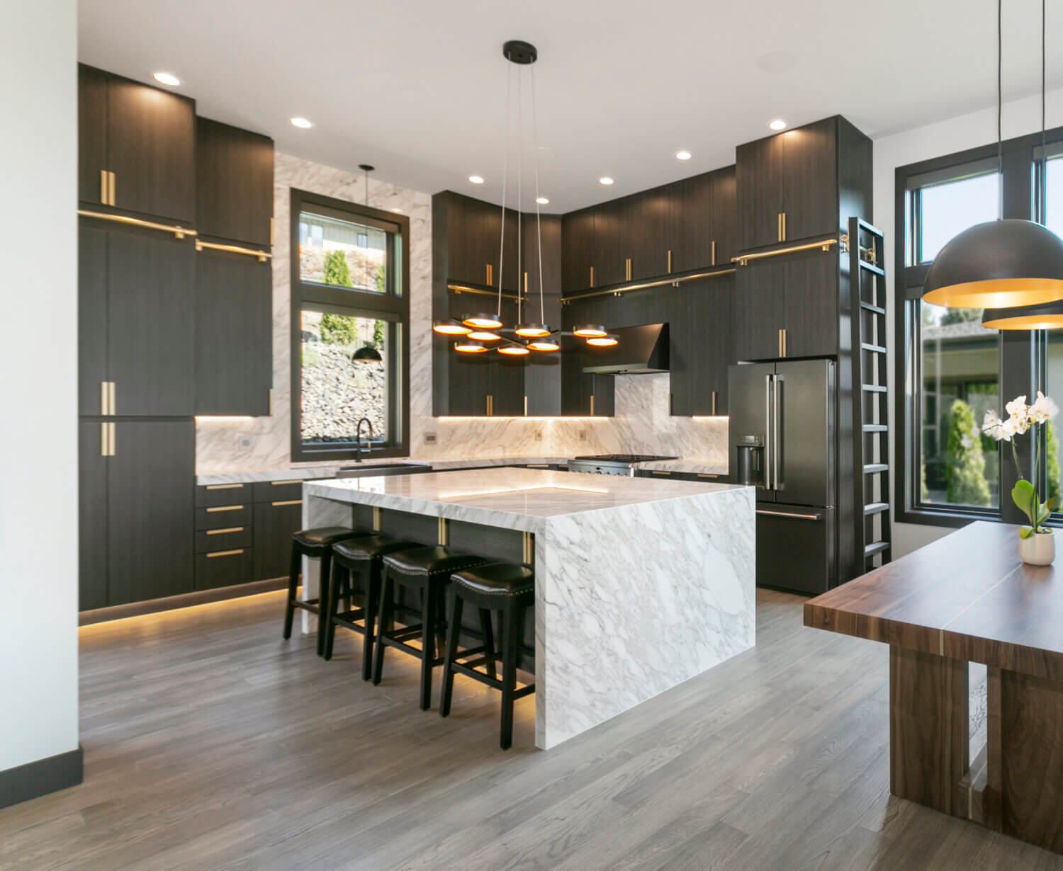 An ultra modern kitchen with contemporary black textured cabinets from Dura Supreme with futuristic lighting details and a wide waterfall kitchen island.