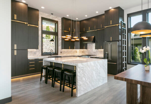 An ultra modern kitchen with contemporary black textured cabinets from Dura Supreme with futuristic lighting details and a wide waterfall kitchen island.