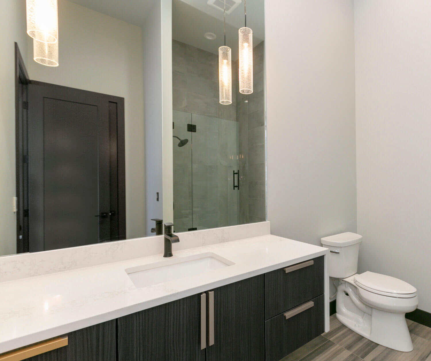 A sleek, modern bathroom design with a black and white color palette and premium contemporary materials and finishes. The long stretching black cabinetry is wall-hung to look as if it’s floating above the bathroom floor delivers heaps of drama to this master bathroom featuring Dura Supreme’s black “Basalt” Textured TFL on the Tempo-Vertical door style.