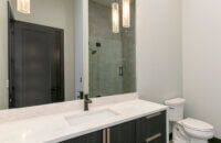 A sleek, modern bathroom design with a black and white color palette and premium contemporary materials and finishes. The long stretching black cabinetry is wall-hung to look as if it’s floating above the bathroom floor delivers heaps of drama to this master bathroom featuring Dura Supreme’s black “Basalt” Textured TFL on the Tempo-Vertical door style.