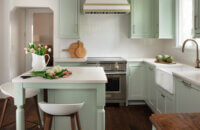 A colorful kitchen with minty green painted cabinets and a white range hood with gold hardware and accents.