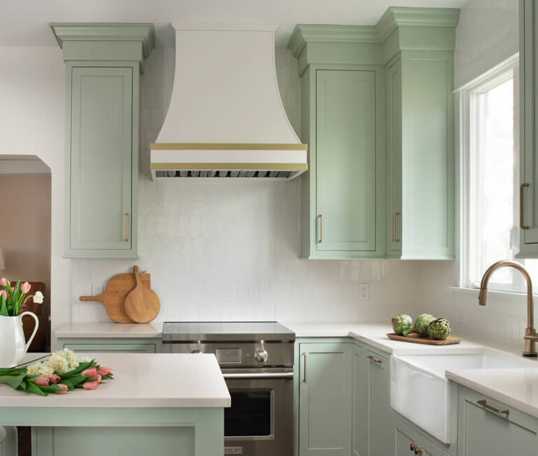 A colorful kitchen with minty green painted cabinets and a white range hood with gold hardware and accents.