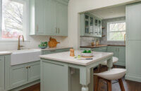 A pastel kitchen with light mint green cabinets , and apron sink, and furniture style kitchen island with Dura Supreme Cabinets.