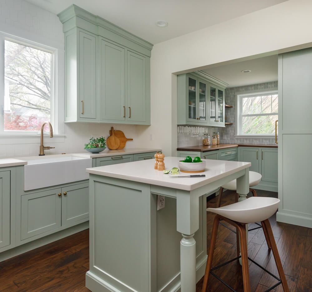 A pastel kitchen with light mint green cabinets , and apron sink, and furniture style kitchen island with Dura Supreme Cabinets.