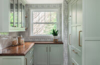 A luxury burtler's pantry with wood countertops and colorful light green painted cabinets.