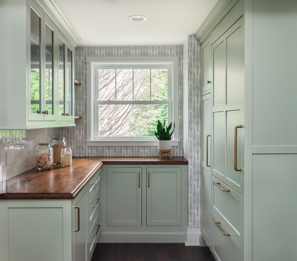 A luxury burtler's pantry with wood countertops and colorful light green painted cabinets.