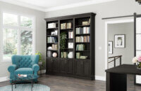 A wall of the home office has a built-in bookcase with cabinets that has a dark stain that matches the office desks.
