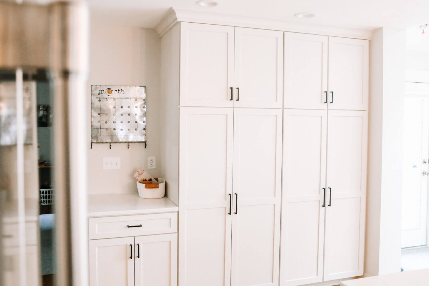 A wall of white painted cabinets and an drop-zone with an organizational planner.