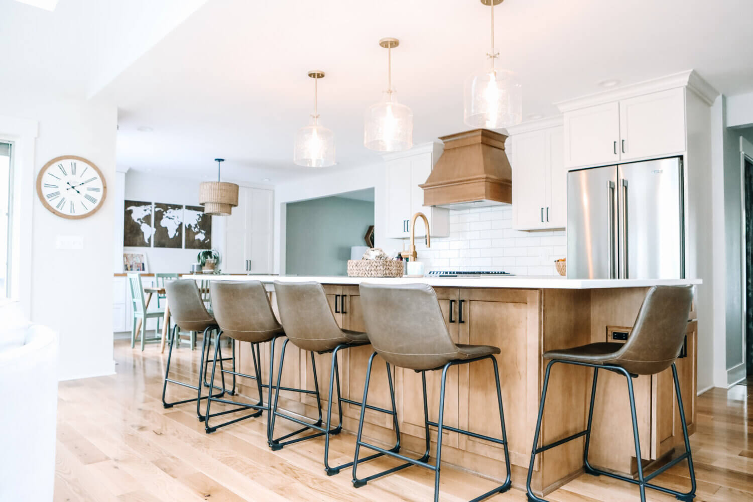An angled view of the kitchen in an open floor plan with a light stained wood kitchen island and wood hood contrasted by white painted cabinets with shaker doors.