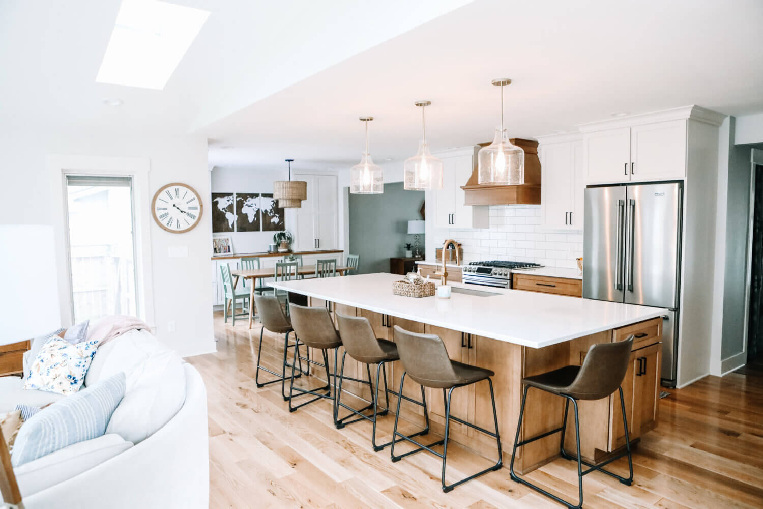 An angled view of the kitchen in an open floor plan with a light stained wood kitchen island and wood hood contrasted by white painted cabinets with shaker doors.