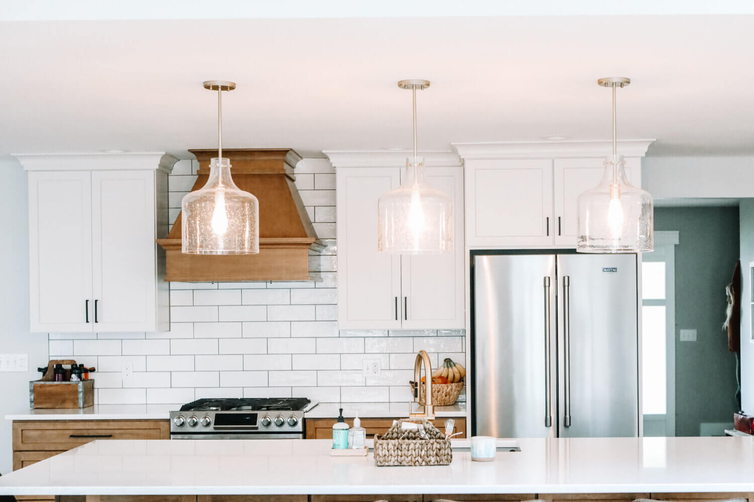 A straight on view of the cooking area of a newly remodeled kitchen with white painted wall cabinets and light stained base cabinets and wood hood.