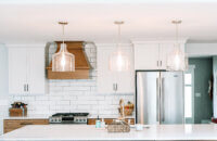 A straight on view of the cooking area of a newly remodeled kitchen with white painted wall cabinets and light stained base cabinets and wood hood.