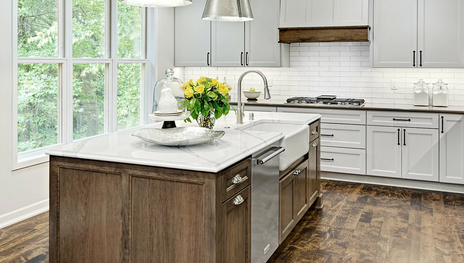 A modern farmhouse kitchen with Dura Supreme's Meridien door style in a true-brown, Caraway stain on Hickory wood for the island and accent on the wood hood paired with Pearl paint for the perimeter cabinets.