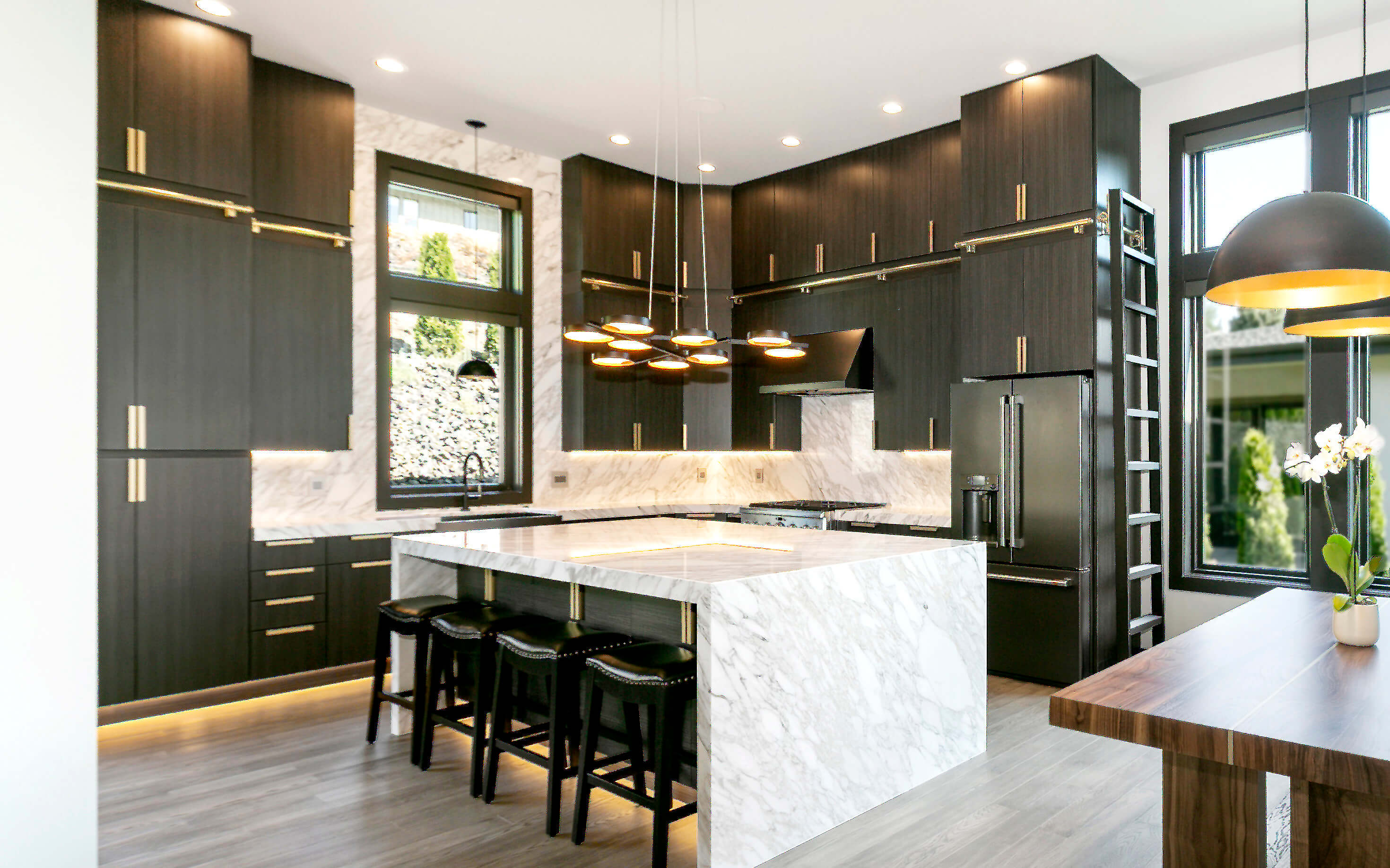 An ultra modern kitchen with contemporary black textured cabinets from Dura Supreme with futuristic lighting details and a wide waterfall kitchen island.