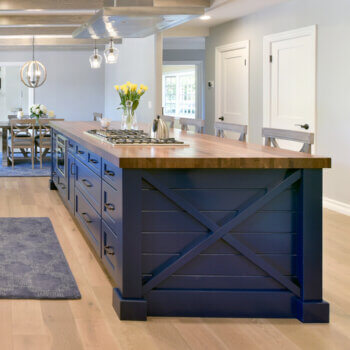 A colorful navy blue kitchen island with an X patterned end cap with shiplap paneling back treatment behind and basic decorative columns on both sides framing the X detail.