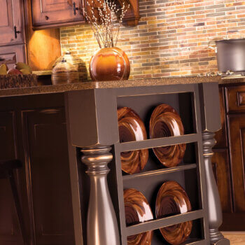 A kitchen island end cap with a decorative plate rack between two large furniture style turned posts in a rustic kitchen design.