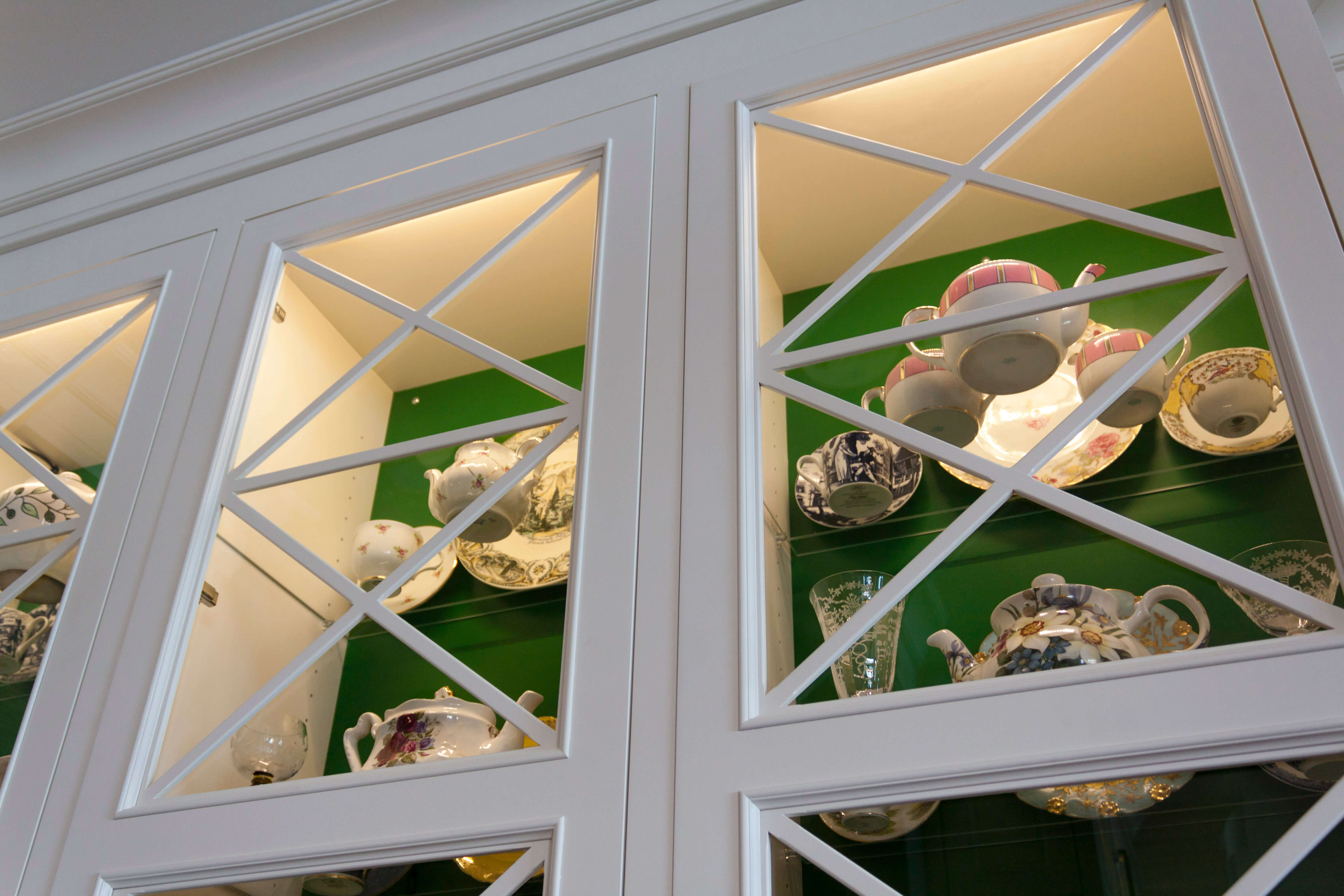 Glass cabinet doors with displayed dishware and decor with an emerald green interior and white painted exterior.