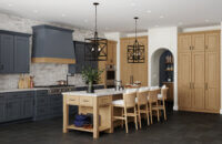 An old Englishh style kitchen design with deep dark navy blue painted cabinets contrasted by light stained cherry wood cabinets. The modern wood hood makes for a stunning focal point with the two toned paint and stain colors. The Dura Supreme kitchen island is a multi-functional workspace with countertop seating for four guests.