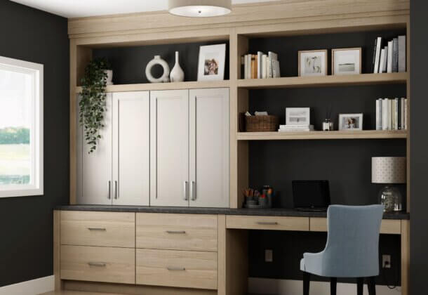 The Dura Supreme office cabinets and built-in desk feature a combination of a slab door style in light stain on the Hickory wood cabinets paired with a detailed flat panel door style in a natural off-white painted finish. This built-in desk and office cabinets were customized to fit the homeowners needs for working from home.