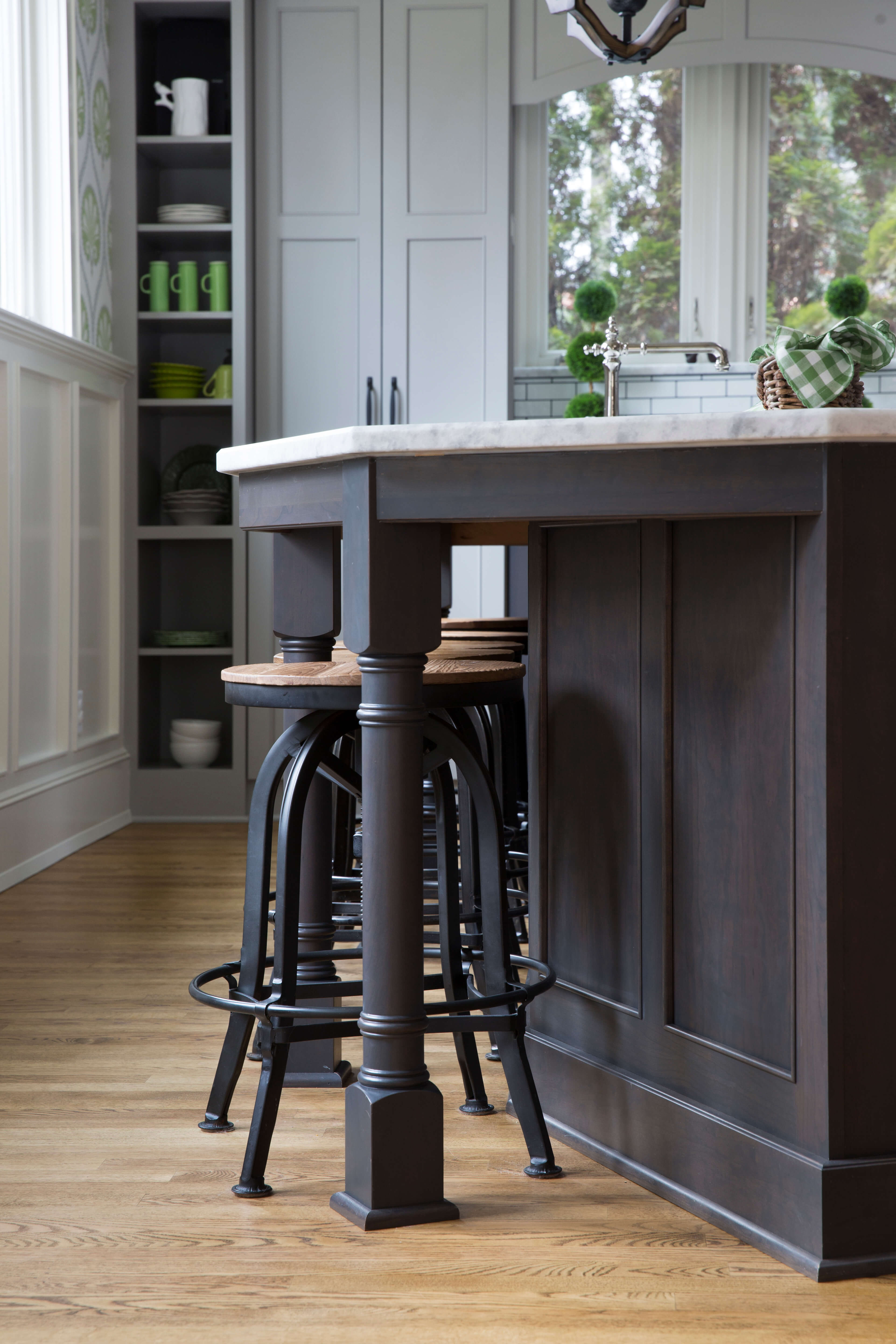 A close up of a gray stained kitchen island and turned post with stool seating.