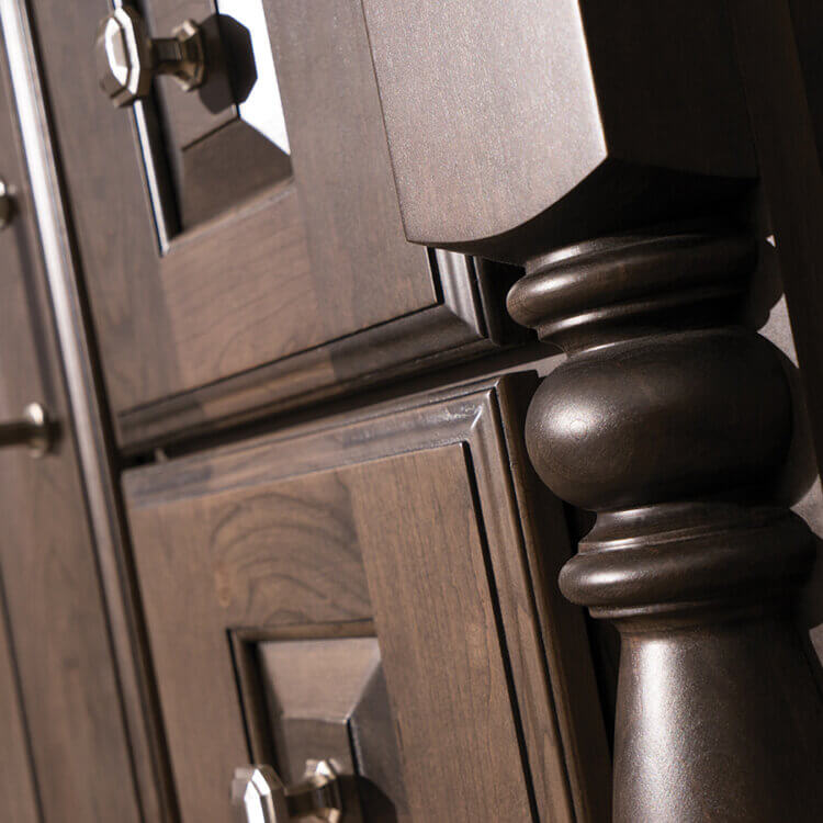 A close up of a turned post on a traditional stlye bathroom vanity with a furniture look. The dark stain on cherry wood is a beautiful choice for the detailed raised panel cabinet doors.