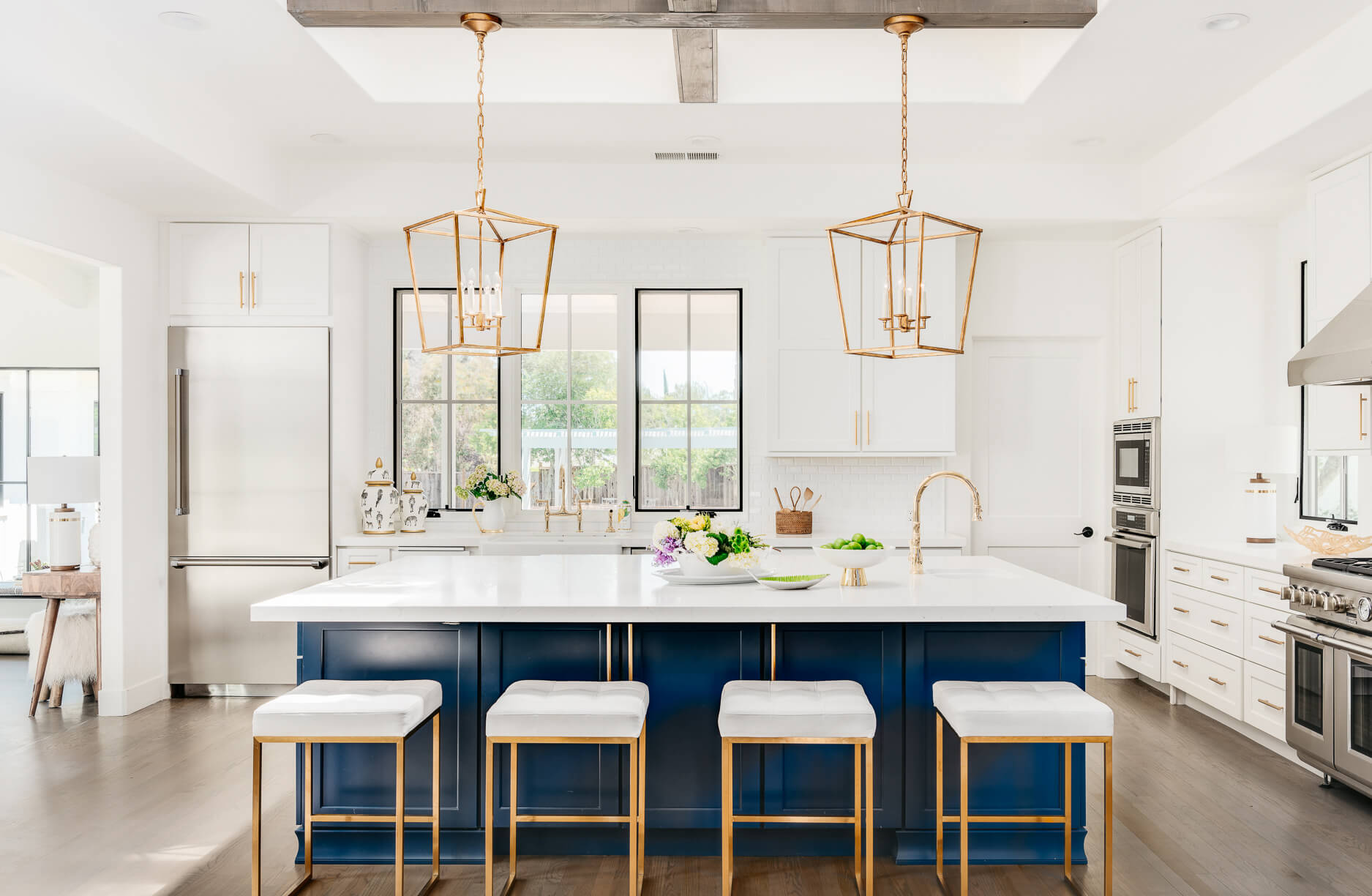 A trendy all white kitchenw ith a bright navy blue kitchen island and gold finishes.