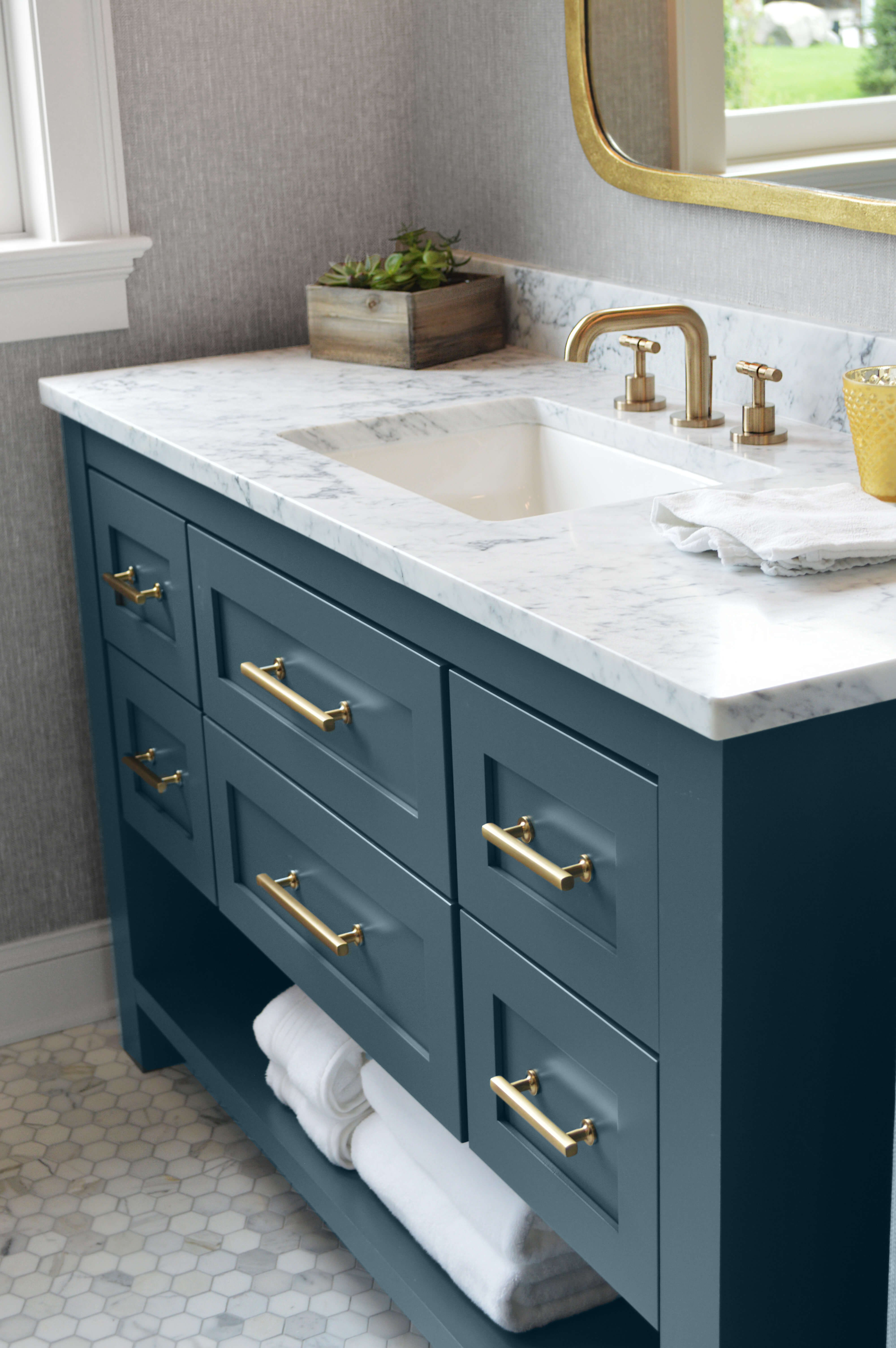 A dark, aqua blue painted bathroom vanity with a furniture style and brushed brass hardware and accents.