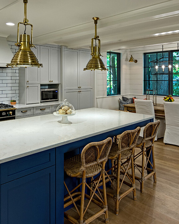 A nautical style kitchen and dining room design with bold navy blue cabinets and antique brass lighting and hardware.