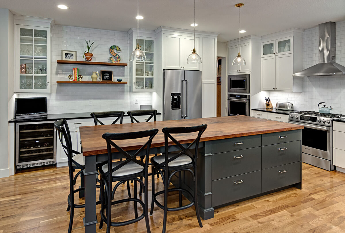 A dark gray painted kitchen island that is half cabinets and half kitchen table style.