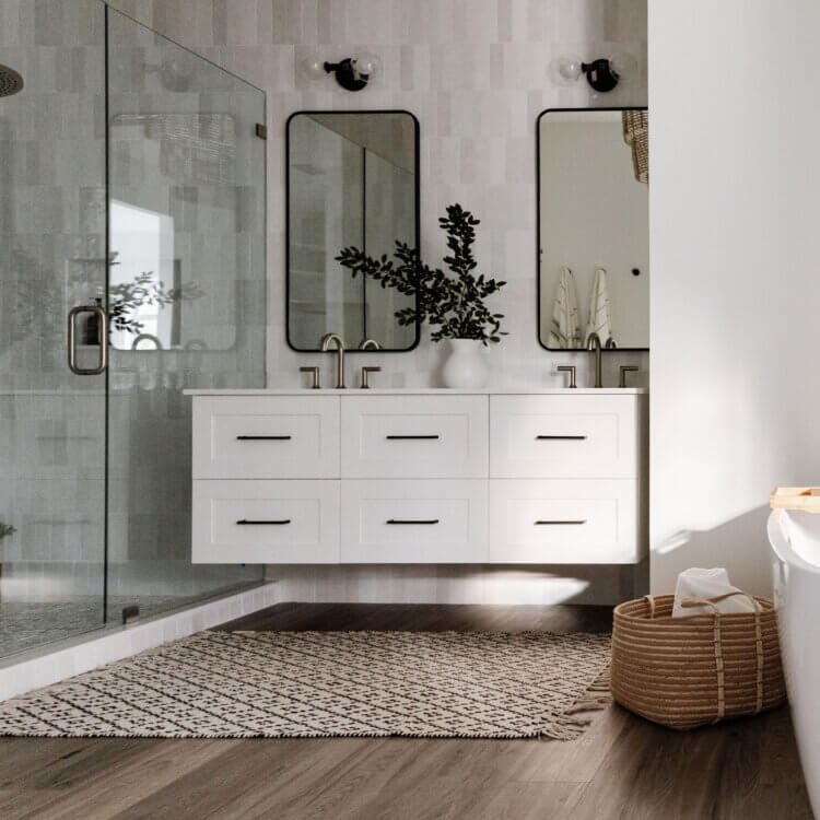 Floating bathroom vanities (also known as wall-hung vanities) are specially constructed, shorter base cabinets that appear to ‘float’ on the wall instead of sitting directly on the floor, thus taking up less visual space. This transitional style master bathroom design uses white painted wall-hung vanity cabinets with a soft color palette and light gray painted walls.