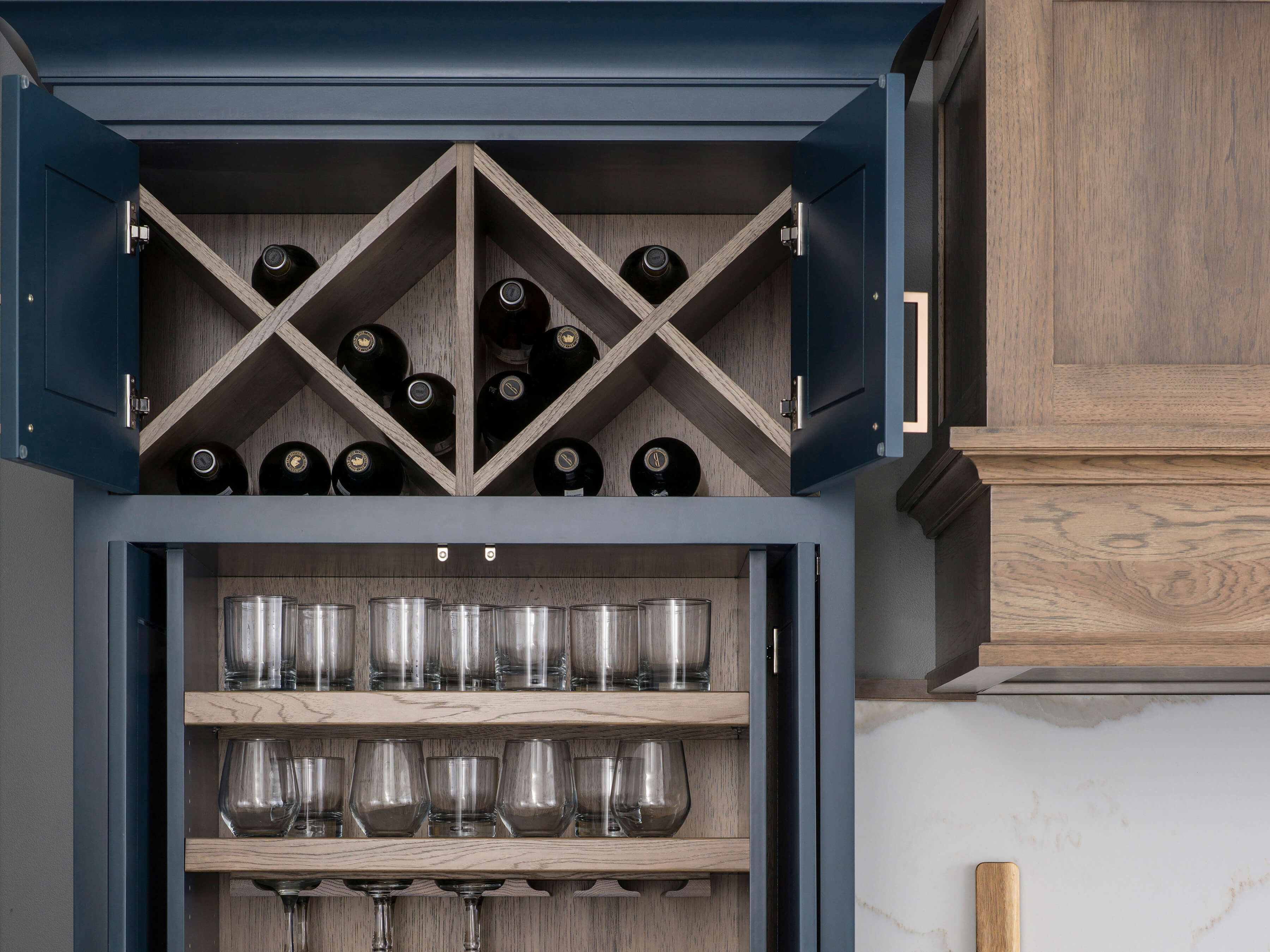 The top of the larder cabinet has two x wine racks up high and out of reach of little ones, as well as plenty of storage for glassware. This modern farmhouse kitchen has two-tone cabinets in a navy blue paint and a medium stained hickory.