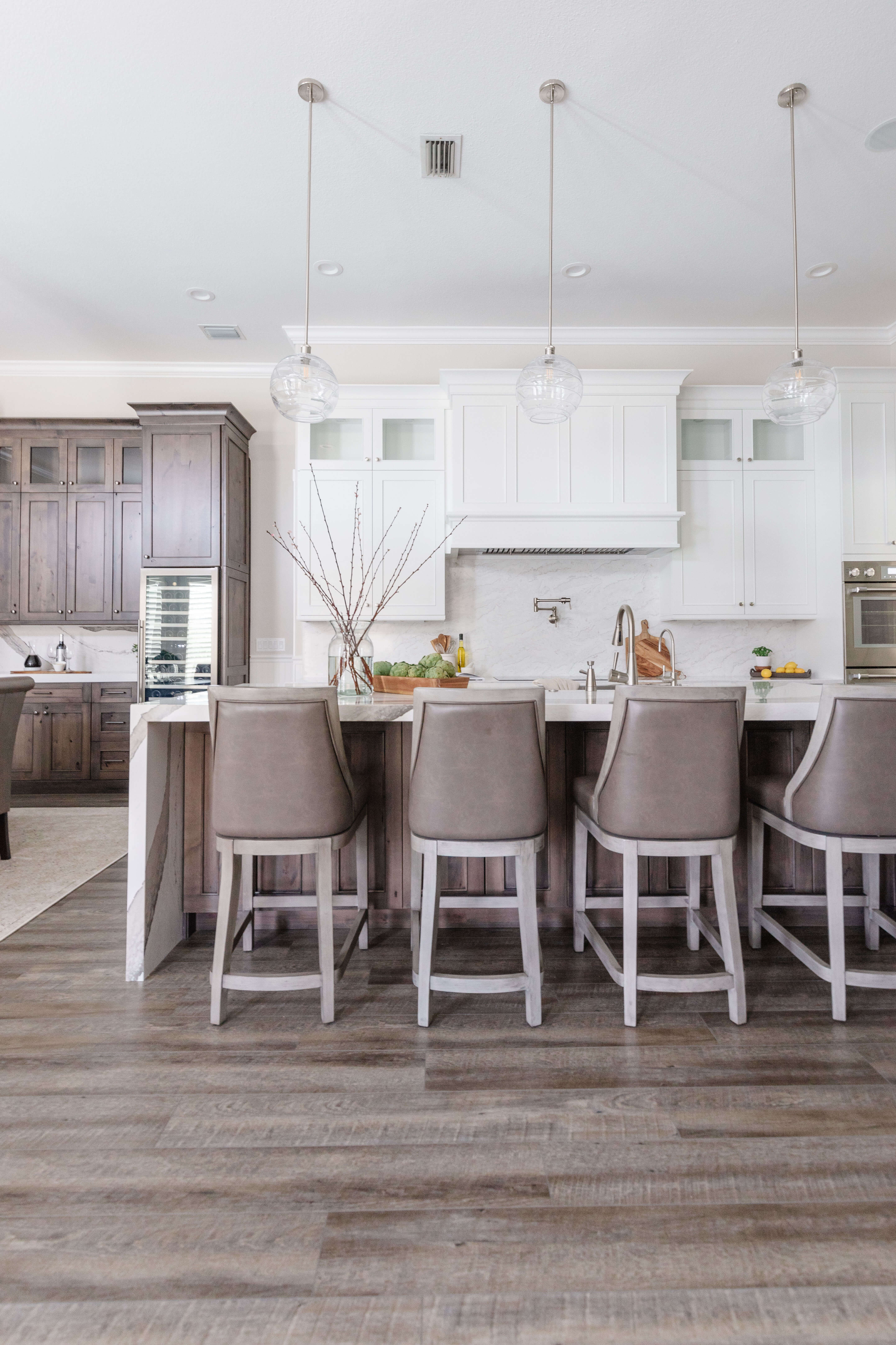This remodel story features a stunning transformation. The new kitchen design is expanded and has lots more storage. The two-tone finshes use a bright white paint for the perimeter and the wood hood and dark stained knotty alder cabinets on the kitchen island and dining room area.