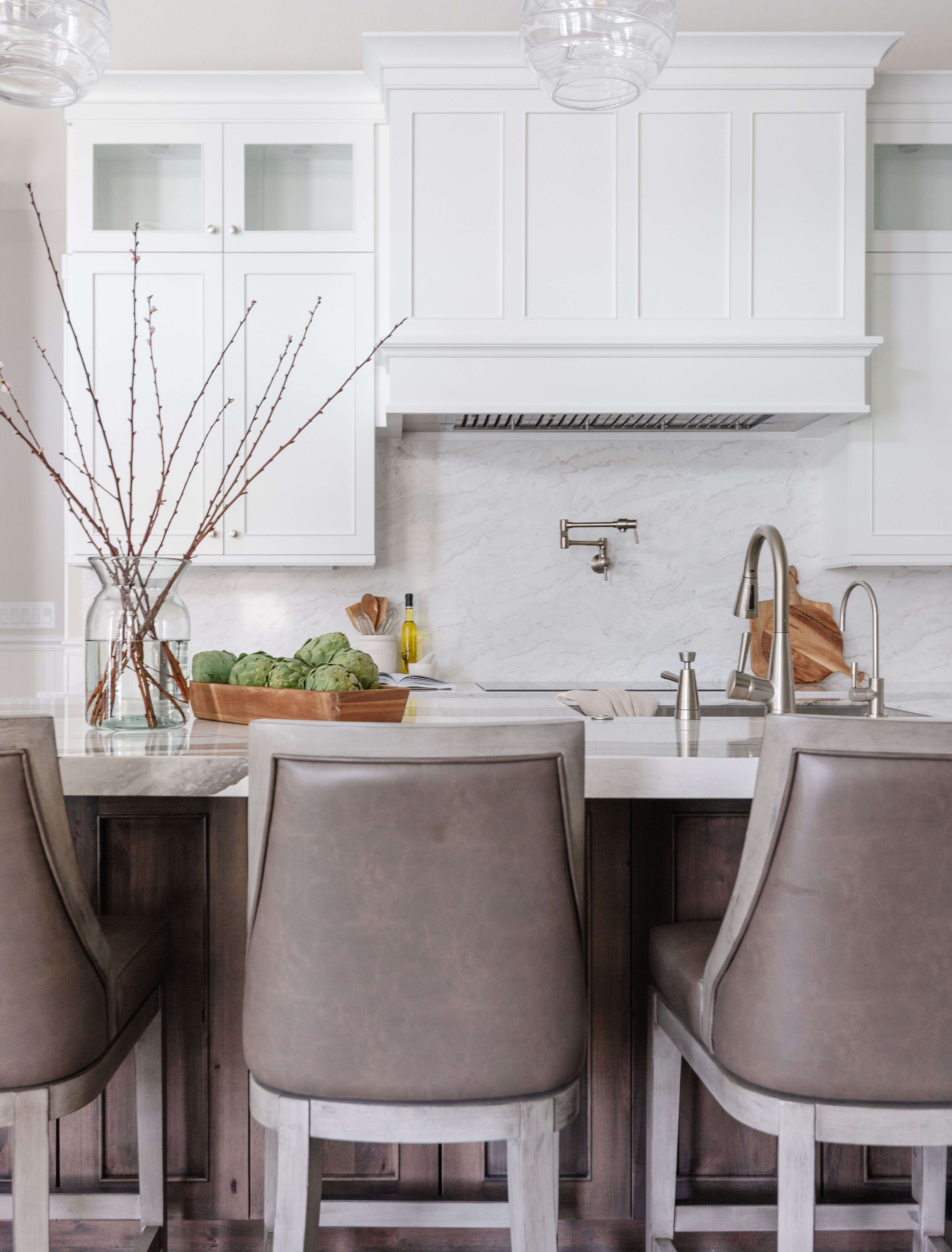 A transitional and casual kitchen design with elegant finishes. A grand white painted wood hood takes center stage over the knotty alder kitchen island.