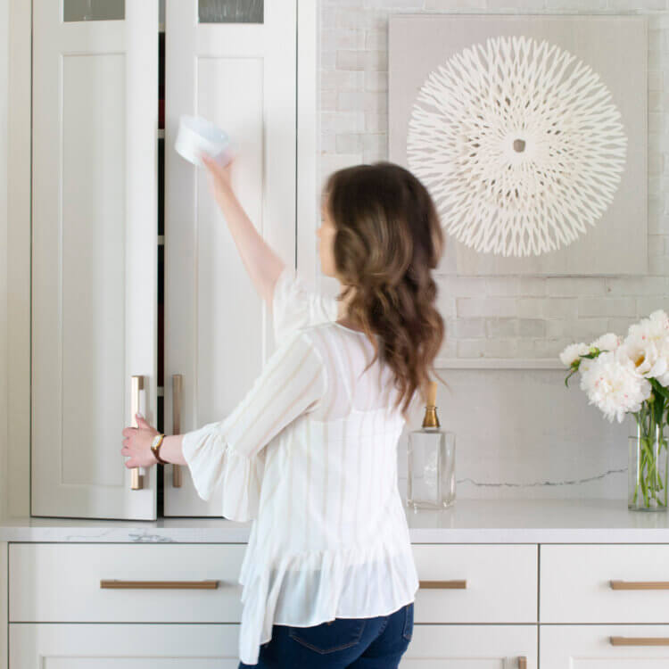 Creative kitchen storage solutions to consider. A homeowner opening a kitchen cabinet in an all-white painted kitchen design.