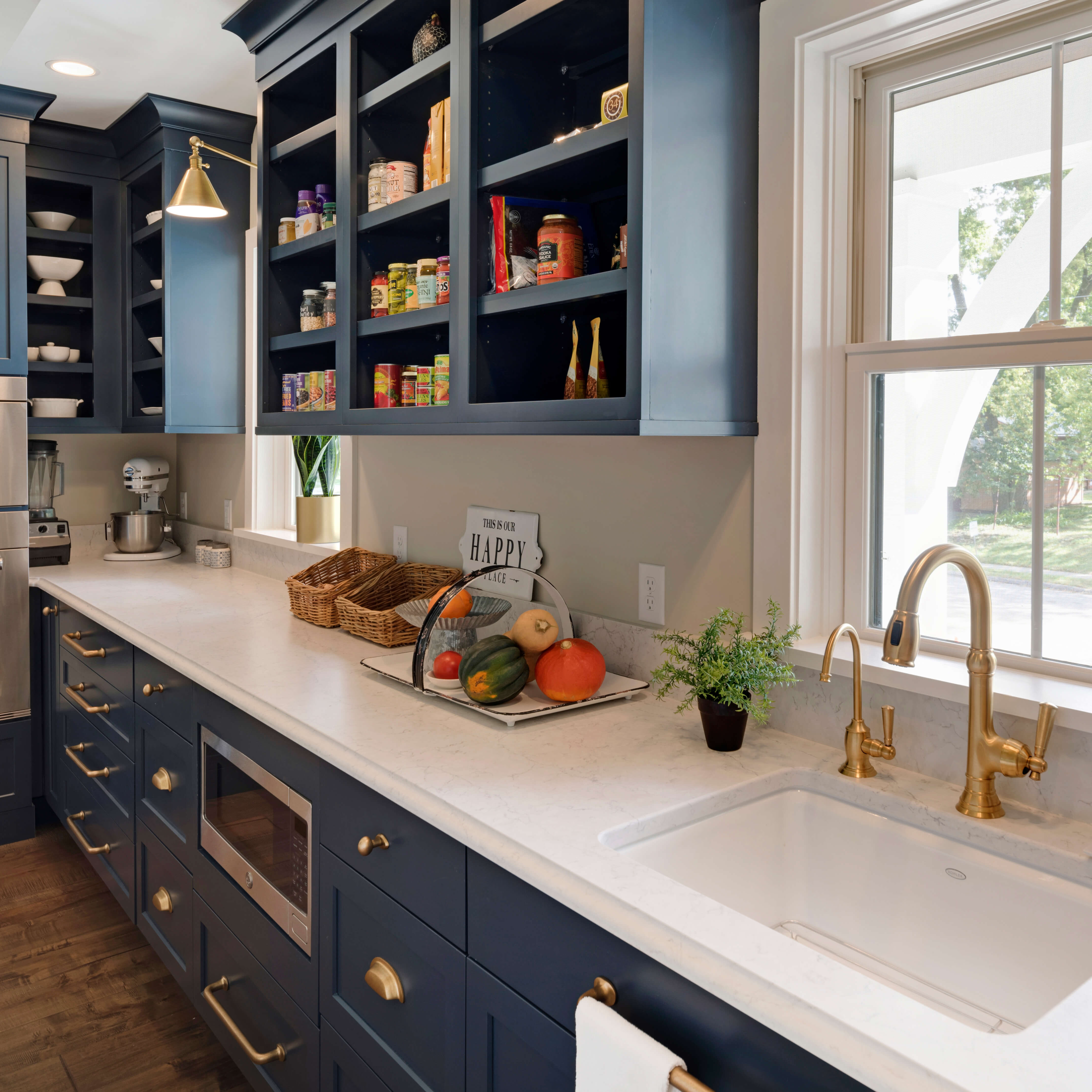 A nautical style butler's pantry with dark navy blue painted cabinets and brass hardware and fixtures.
