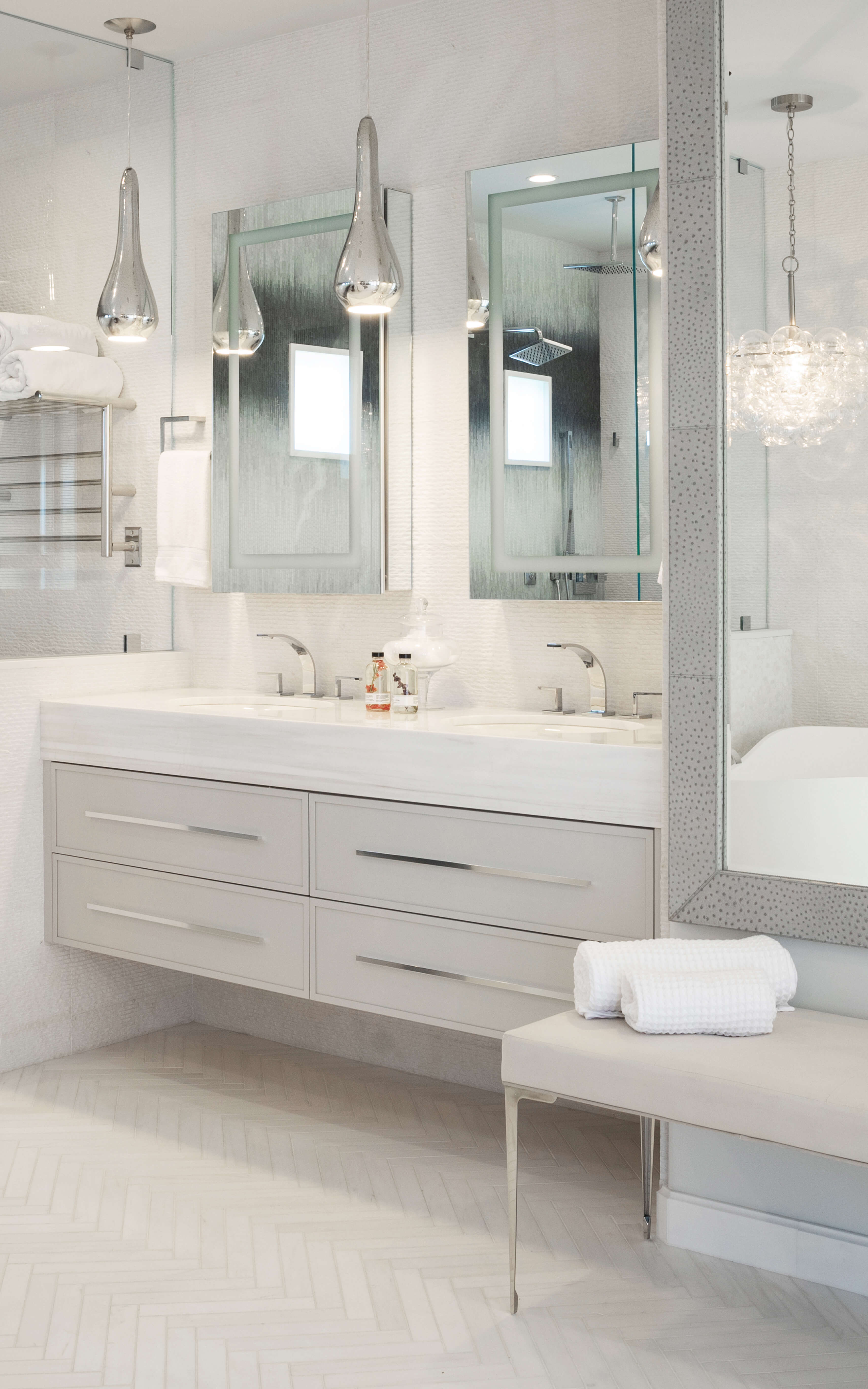 A glamourous master bathroom suite with a floating vanity with very thin profiles on the flat panel door. The wall hug vanity is shown with a soft, light gray painted finish, long satin nickel hardware pulls, and a thick quartz countertop.